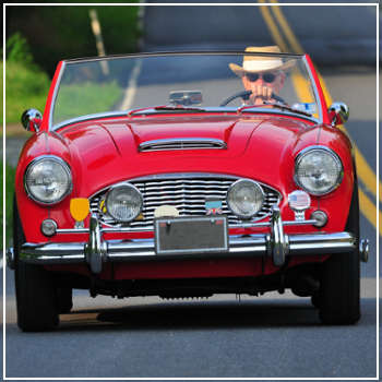 older man driving a red vintage car