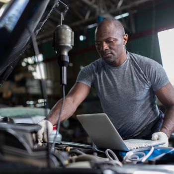 mechanic using computer to diagnose car engine issue